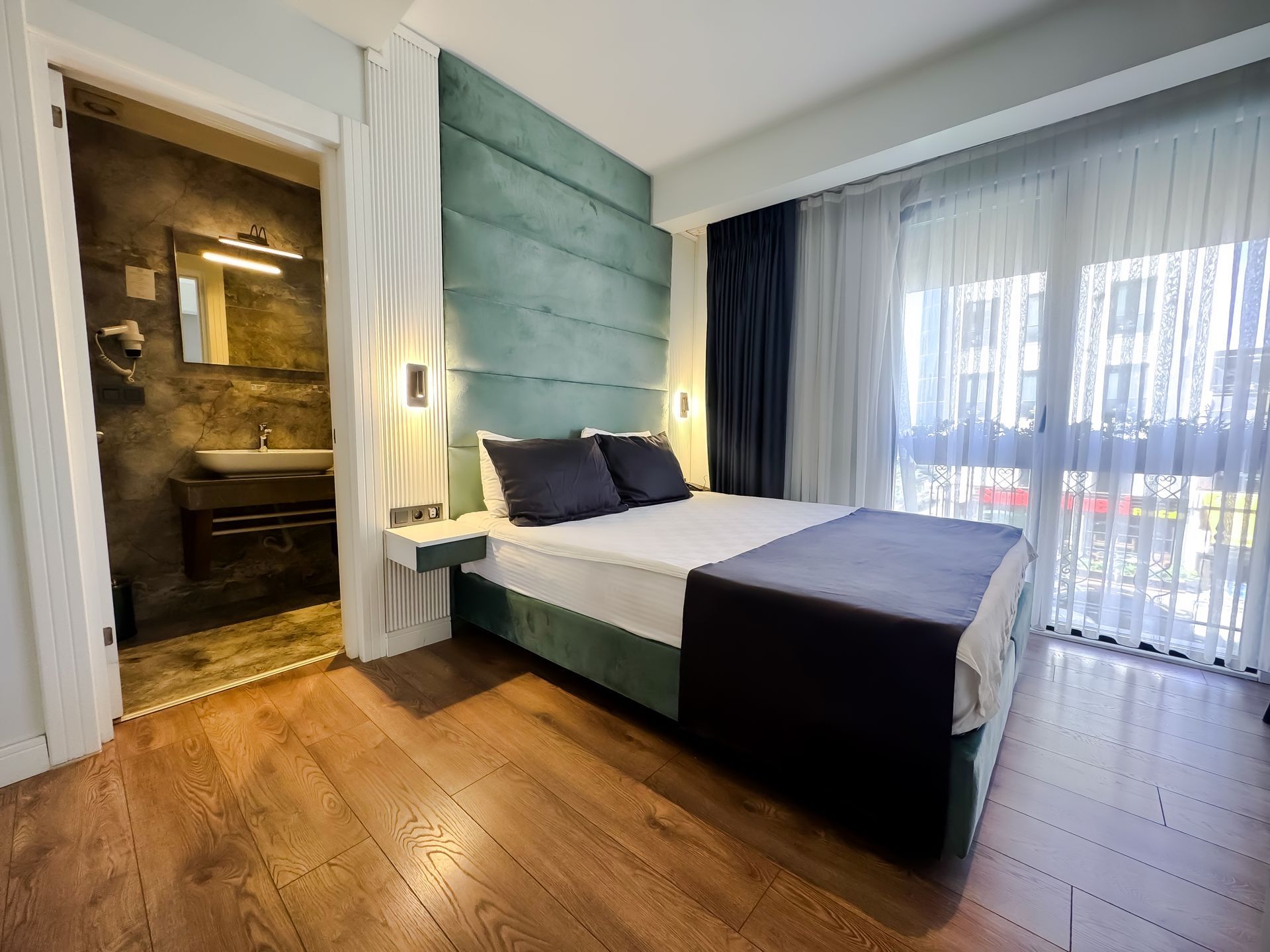 Modern bedroom with teal paneled wall, bed, wood floor, and large window with sheer curtains
