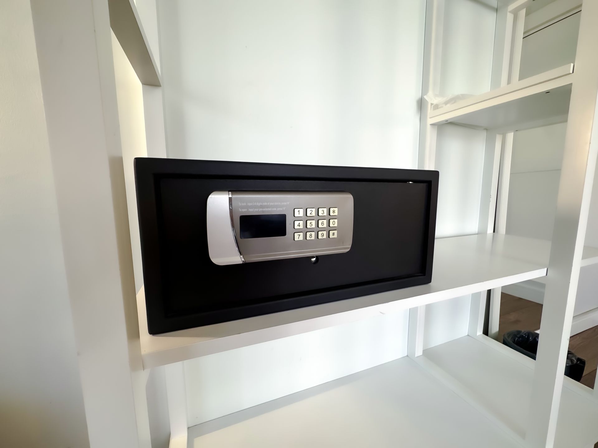 Black wall-mounted safe with keypad on white shelf in a closet