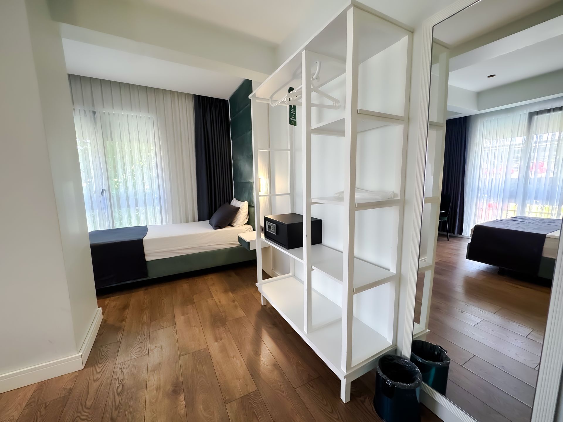Bright bedroom with two beds, white shelving divider, and wood floors, seen from a hallway.