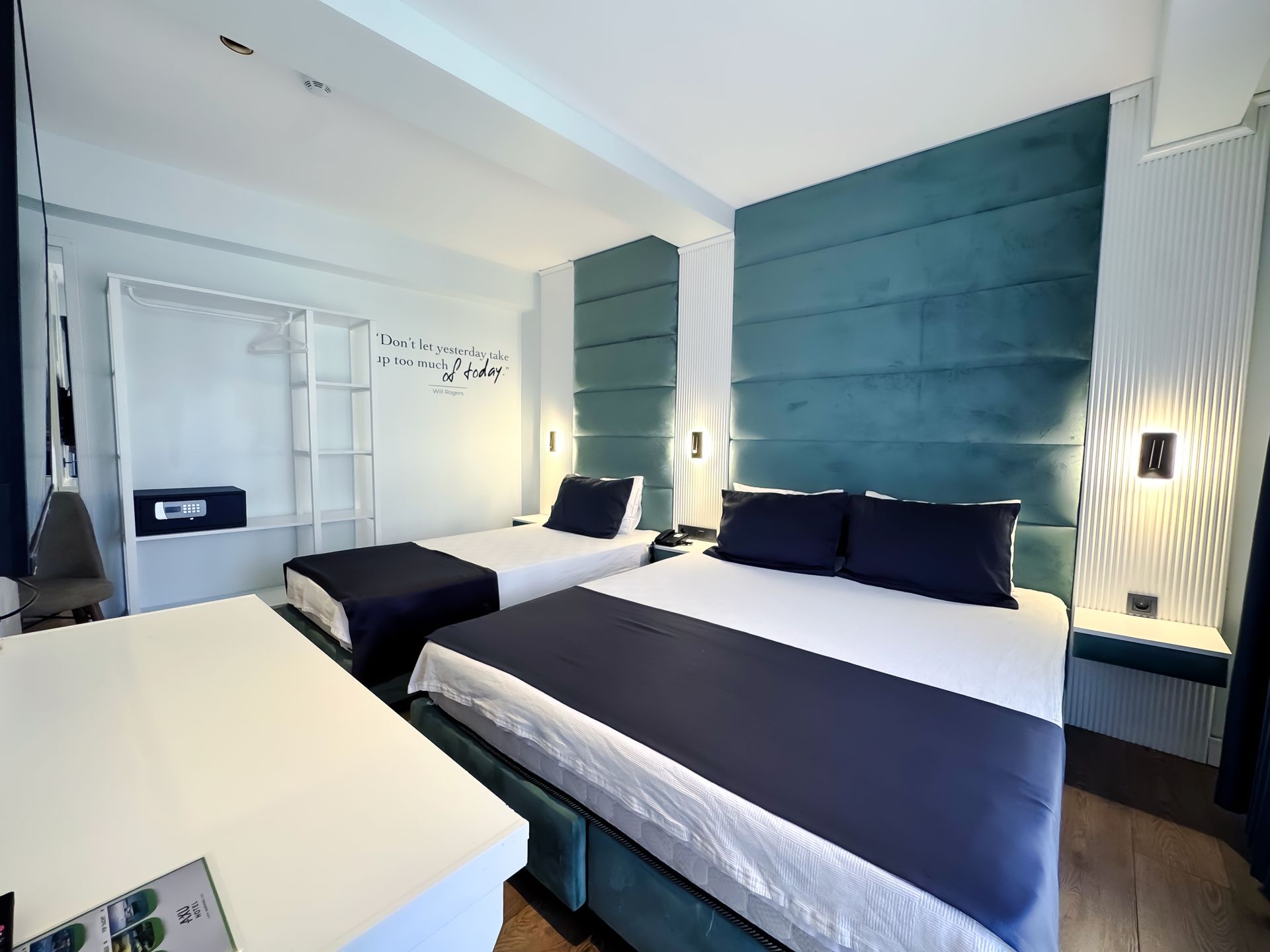 Modern hotel room with twin beds, teal headboards, wall lamps, and white bedding