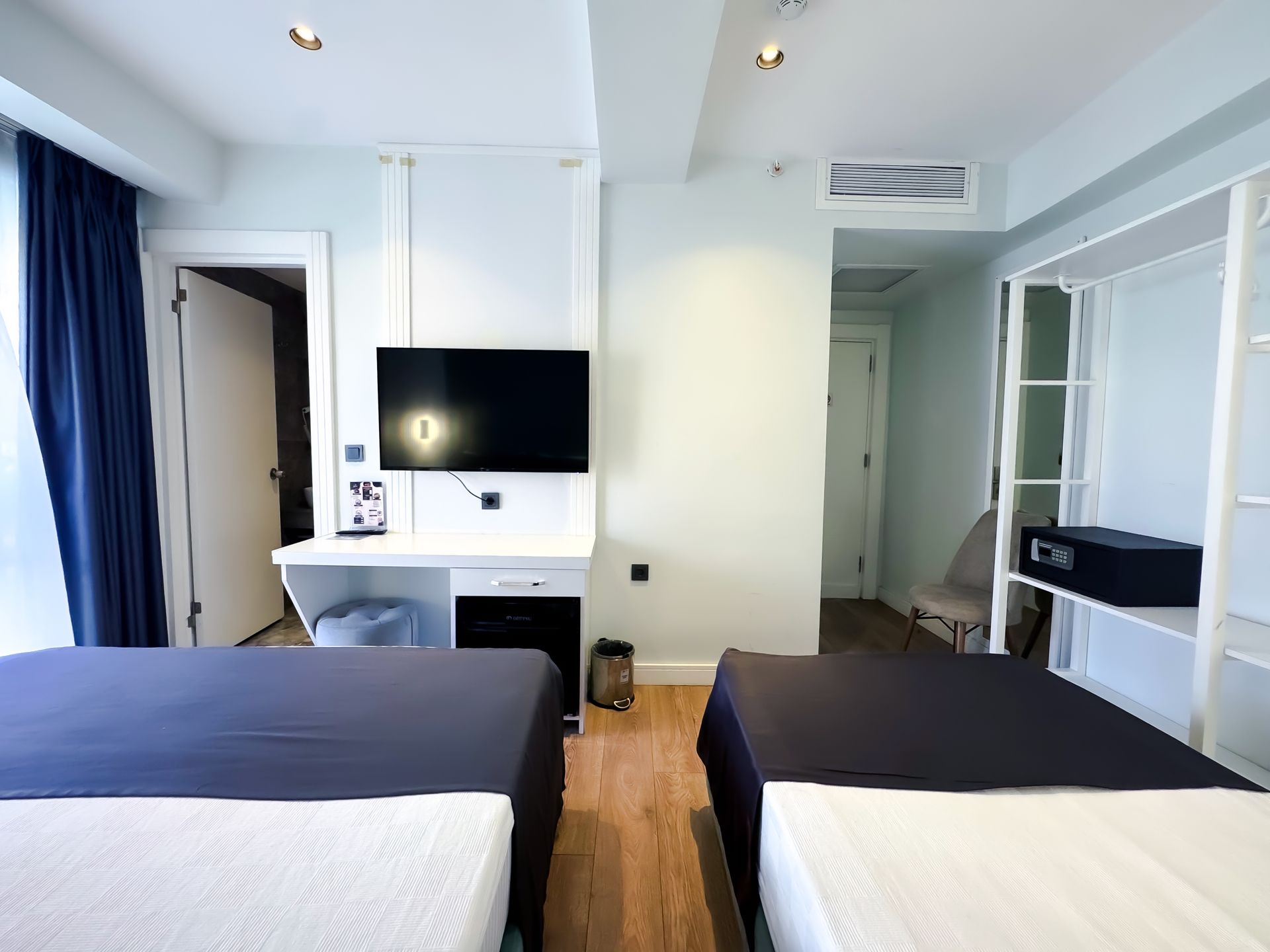 Modern hotel room with two beds, desk, wall TV, and large window with curtains