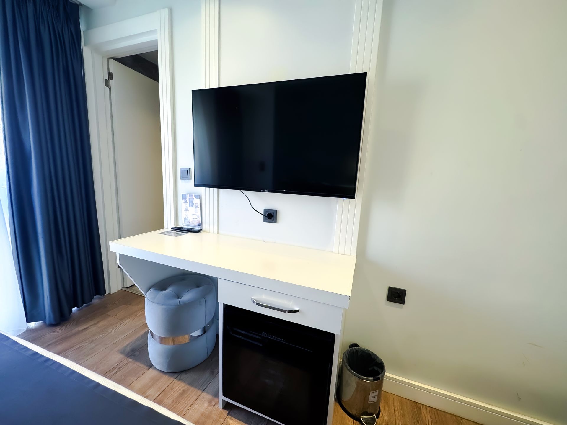 Small room with wall-mounted TV, desk, chair, and curtain by a doorway