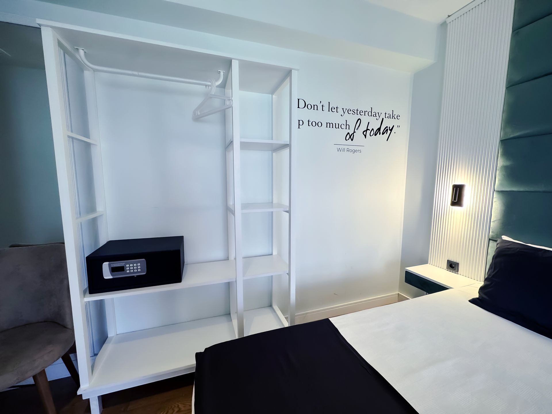 Bright white bedroom with open closet shelves, black bench, bed, and wall text above the headboard.