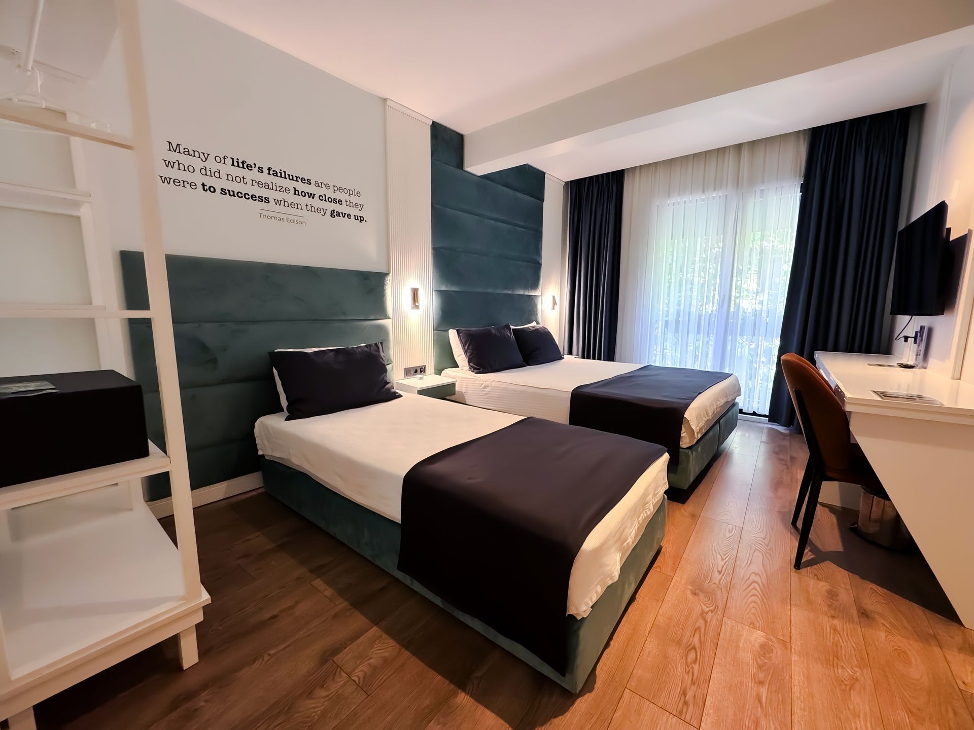 Modern hotel room with two twin beds, dark blue accents, desk, and large window with curtains