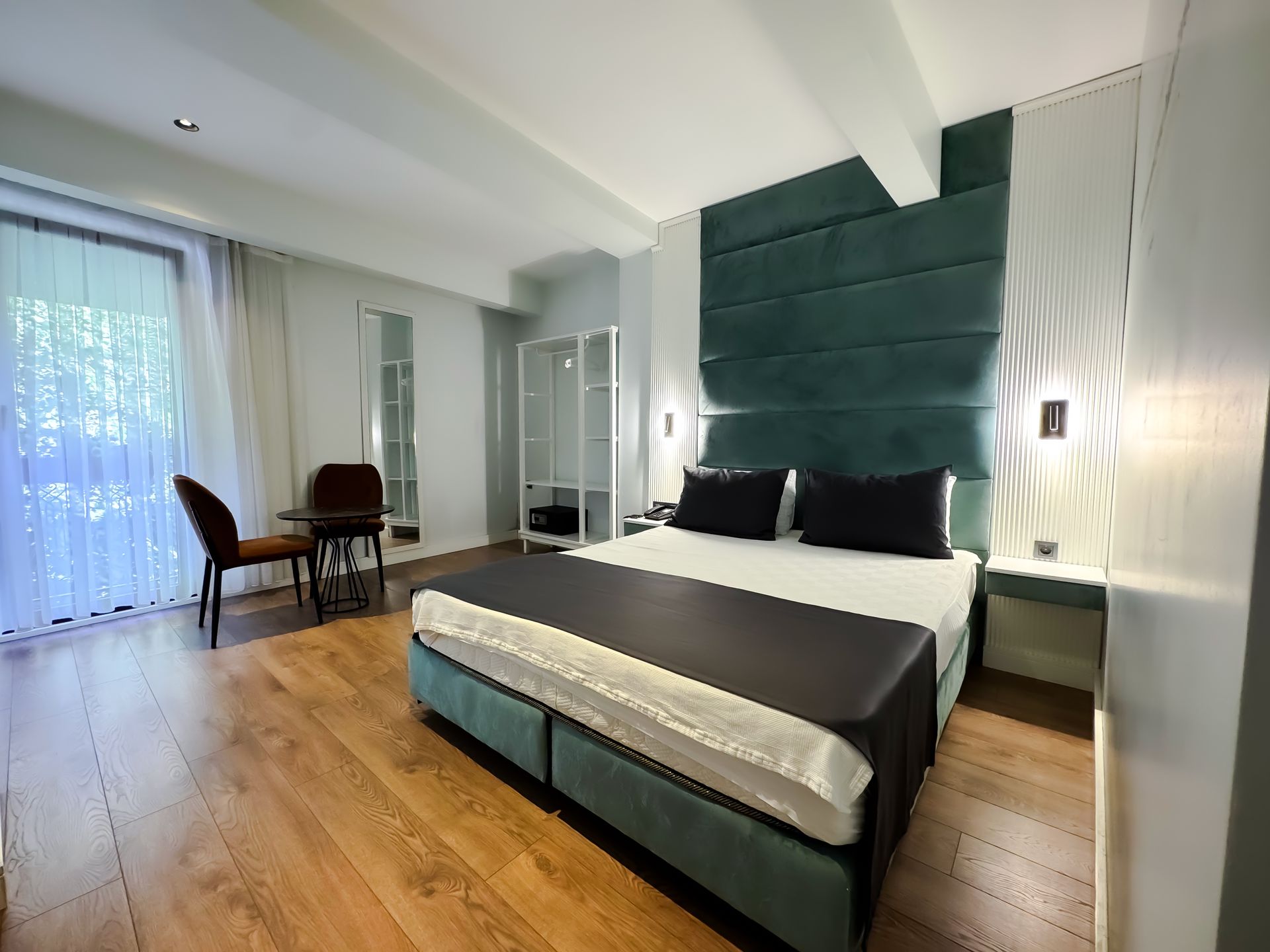 Modern bedroom with teal upholstered bed, wood floors, desk by window, and mirrored closet doors