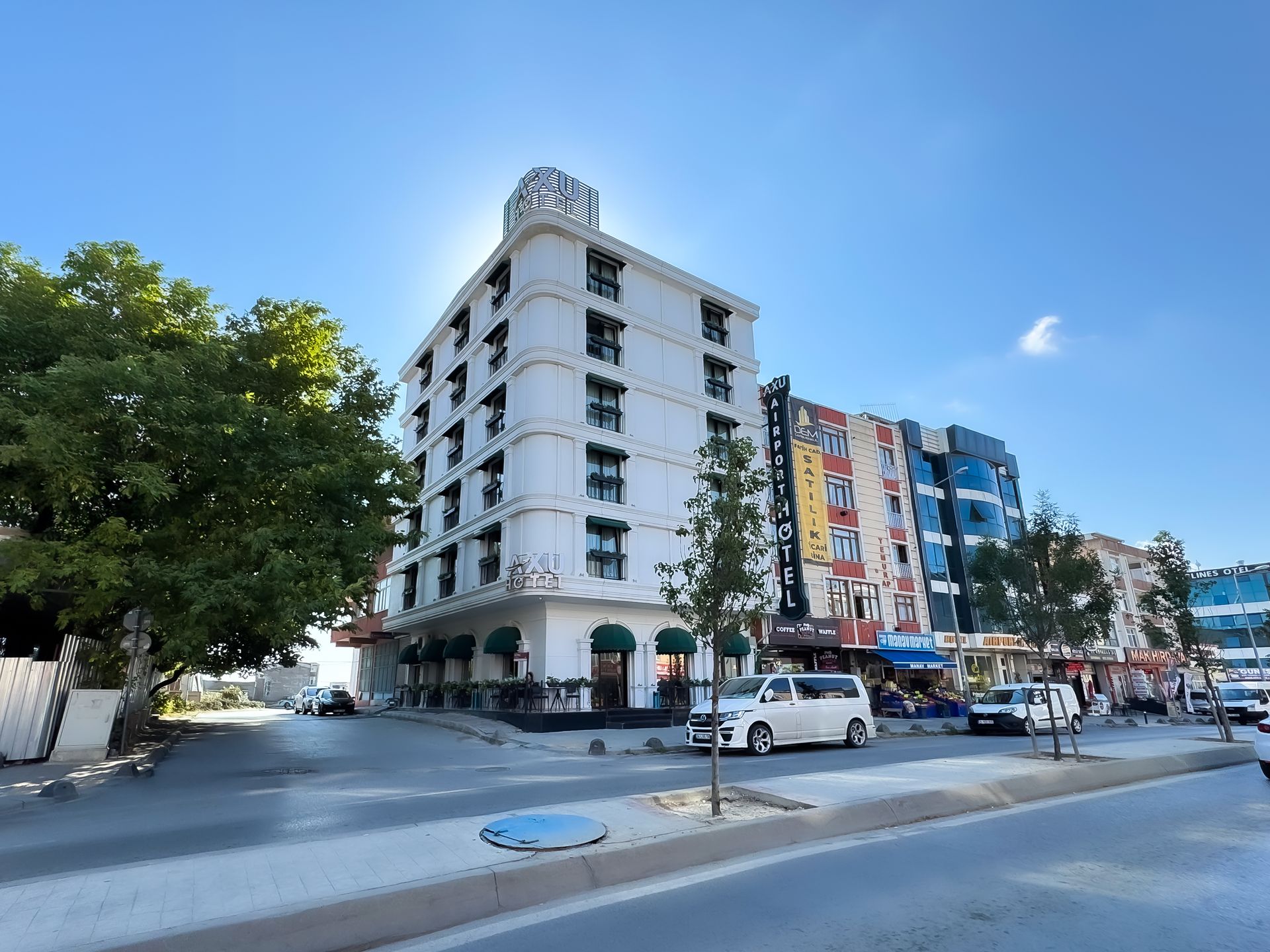 White corner building beside a colorful mural-covered building on a sunny city street with cars.