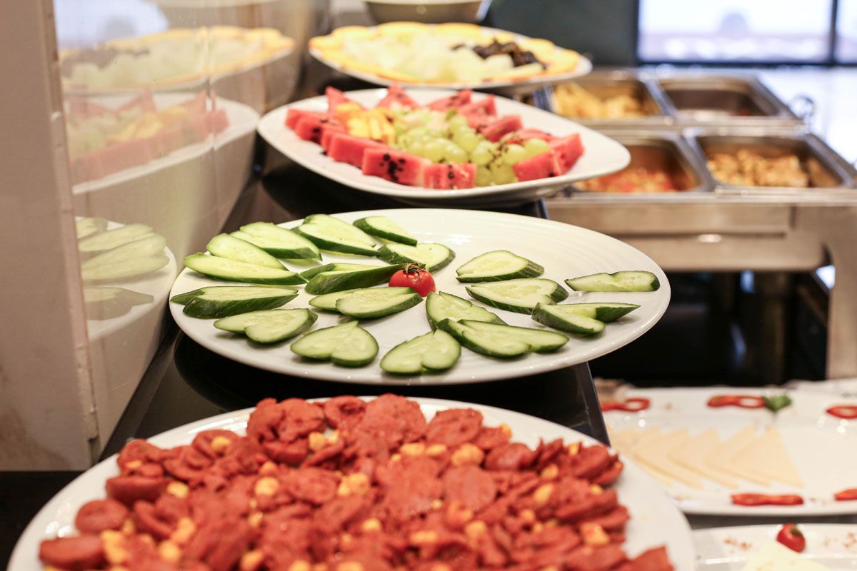 Buffet table with sliced cucumbers, fruit, and a tray of roasted peanuts in a serving area