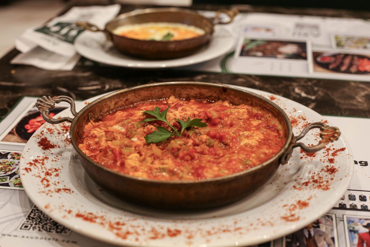Two bowls of baked dish with herbs on a newspaper-covered table, front bowl in focus
