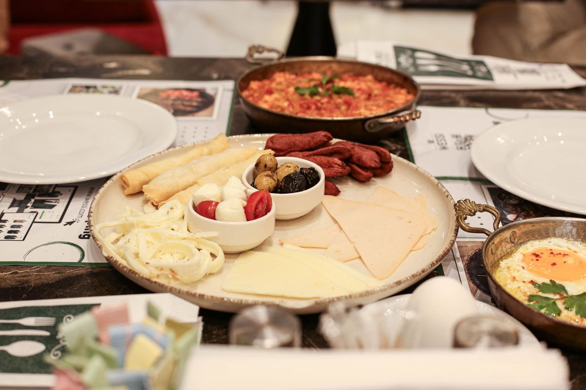 Breakfast spread with omelet, fruit, sausages, bread, and soup on a dining table