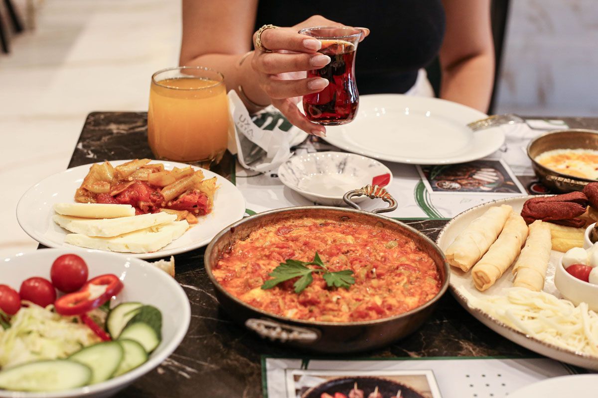 Person holding a glass at a table with assorted Mediterranean dishes, including salad, dips, and flatbread.