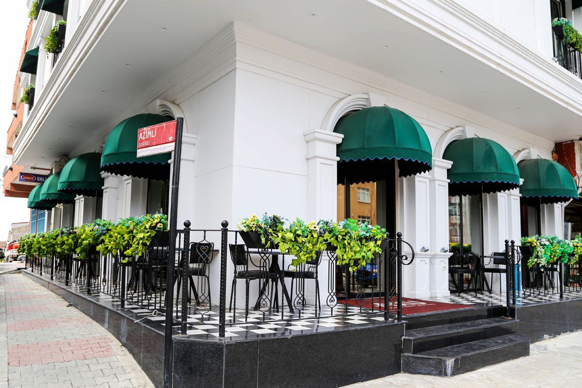 Corner café with green awnings, black railings, and outdoor seating on a sidewalk corner