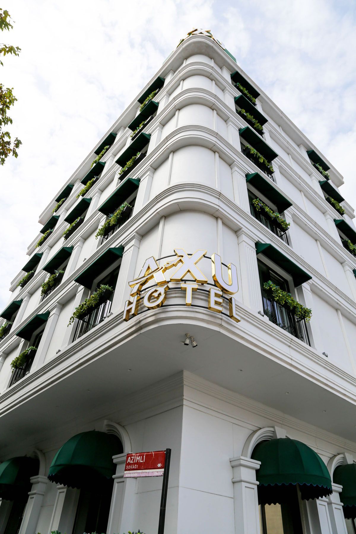 White corner hotel building with green awnings and balconies, viewed from below