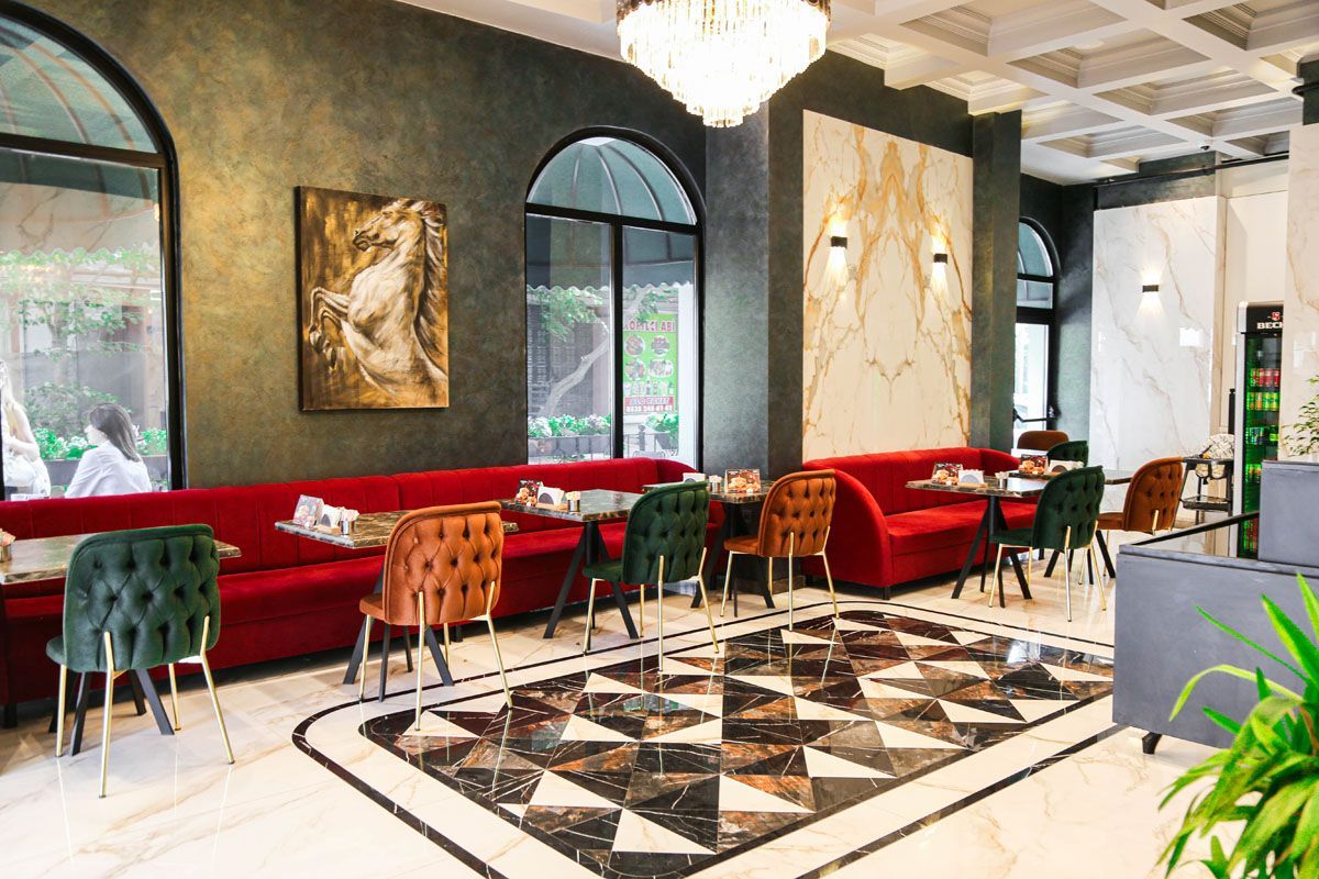 Modern lounge with red sofas, colorful chairs, and black-and-white tiled floor under arched windows