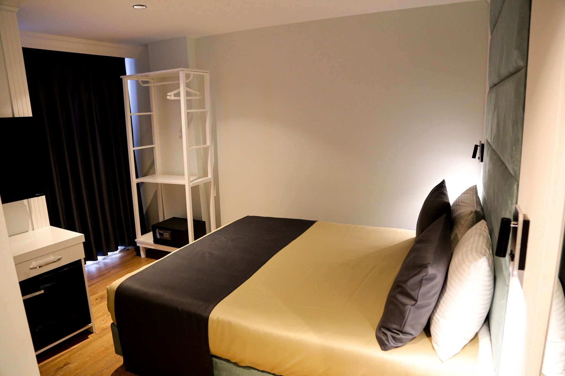 Modern hotel room with a bed, desk, white shelving, and soft lighting