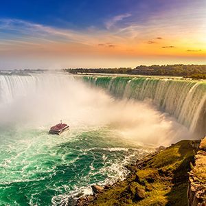 A boat is going down the niagara falls at sunset.