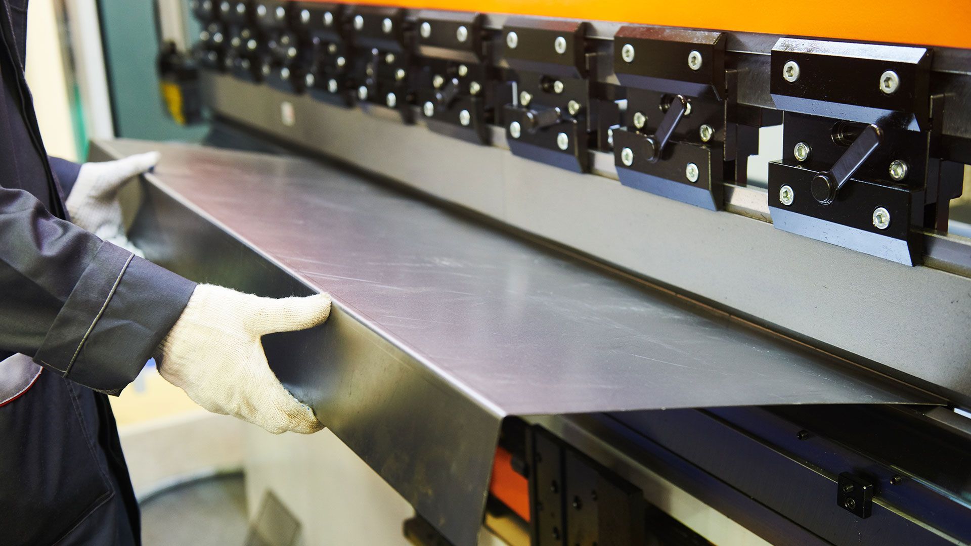 A worker is bending a piece of metal on a brake press. 