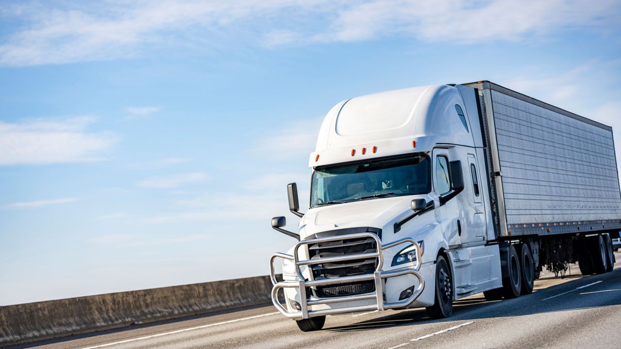 A white semi truck is driving down a highway for just in time delivery.