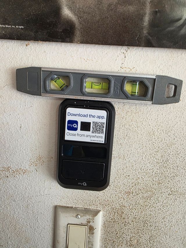 Tape measure and level placed above a wall-mounted device and electrical outlet on a painted wall.