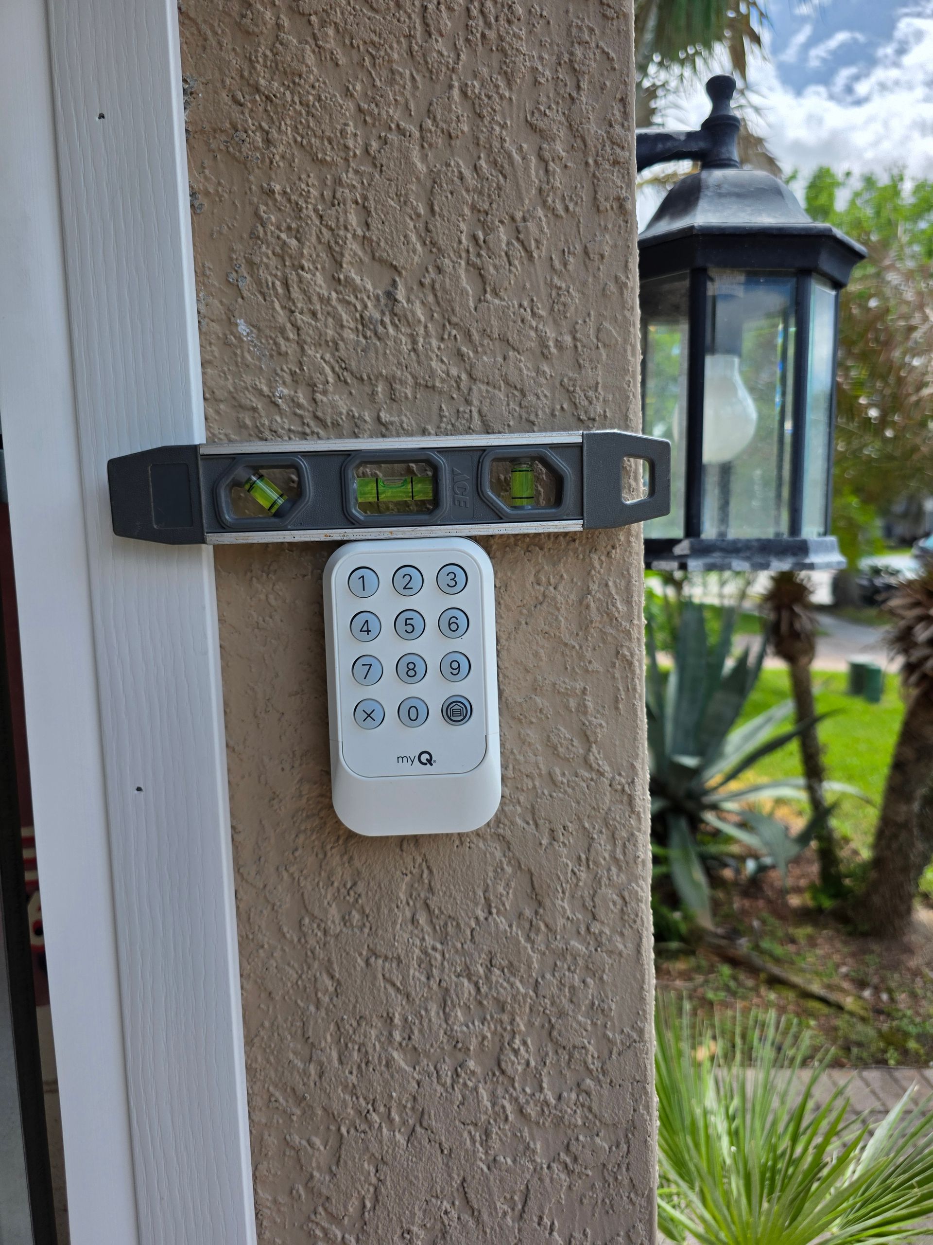 Small keypad and spirit level mounted on a stucco wall beside a lantern.