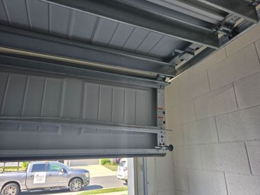 Open garage door with gray metal panels and a parked car visible outside, beside a cinder block wall