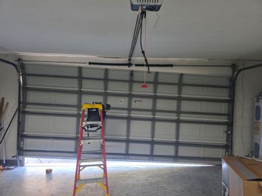 Garage with closed overhead door, red ladder, and ceiling-mounted garage door opener.