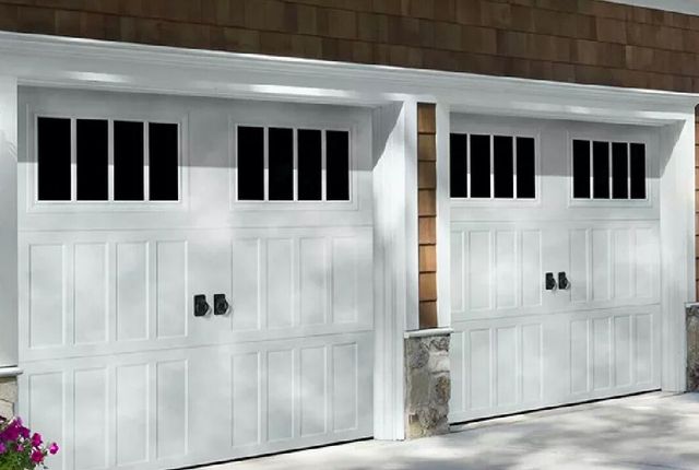 Two white garage doors with black window panes on a tan house exterior
