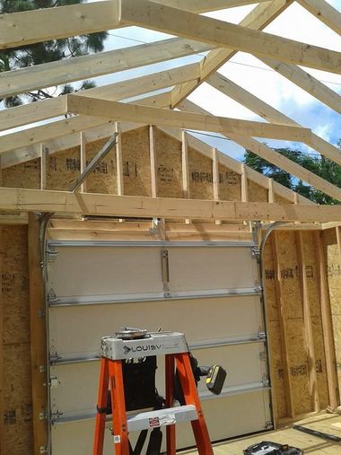 Partially built garage frame with roof trusses and a ladder inside under construction