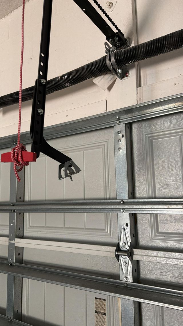 Black garage door opener arm and red emergency release cord over a closed gray garage door.