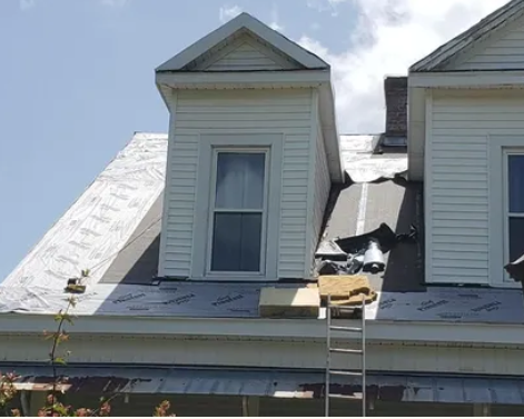 Roof with storm damage and a ladder leaning against a white house dormer
