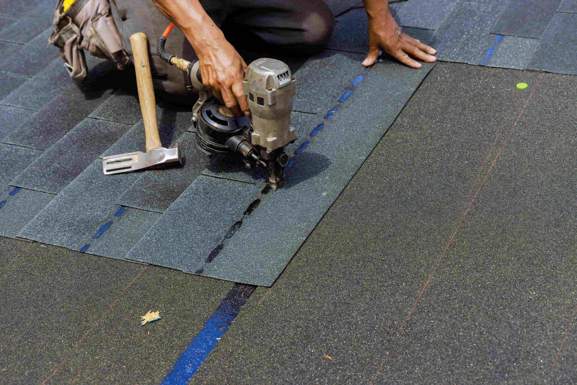 Worker in yellow hard hat repairing red roof tiles with tools near a window