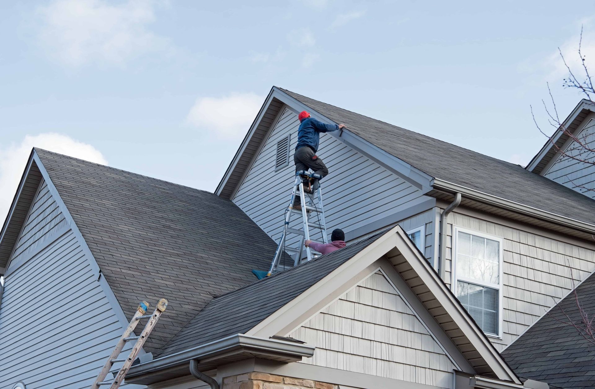 Roofer in yellow hard hat seals a cracked brown tile roof with a caulking gun