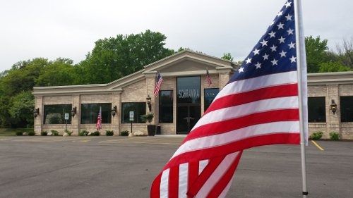 American flag in foreground, brick building with large windows in background.