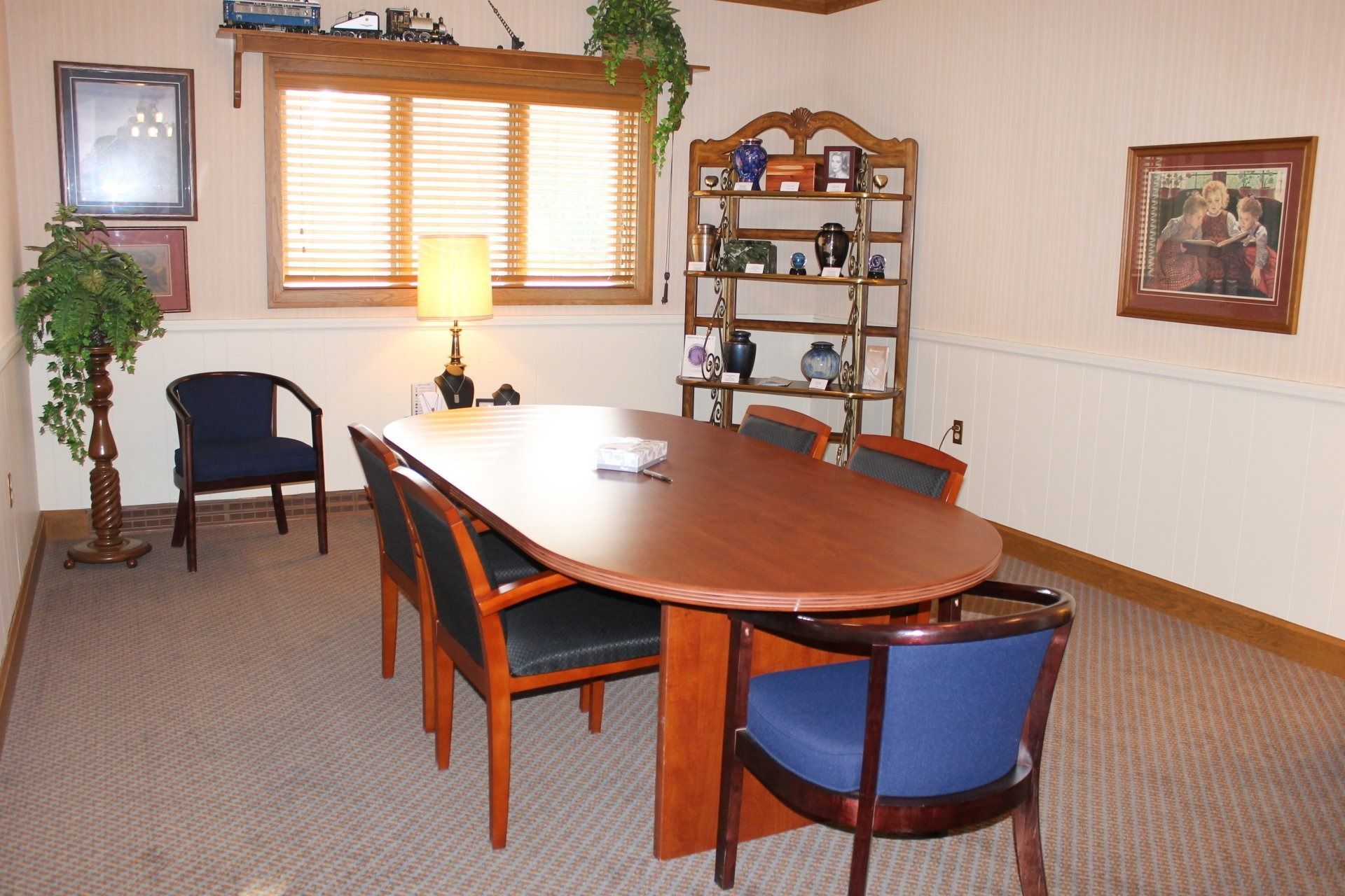 Meeting room with oval table and chairs, window, shelves with items.