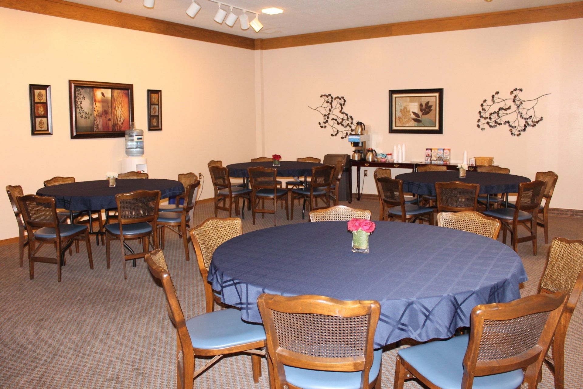 A room with round tables covered in blue tablecloths, chairs, and artwork on the walls.