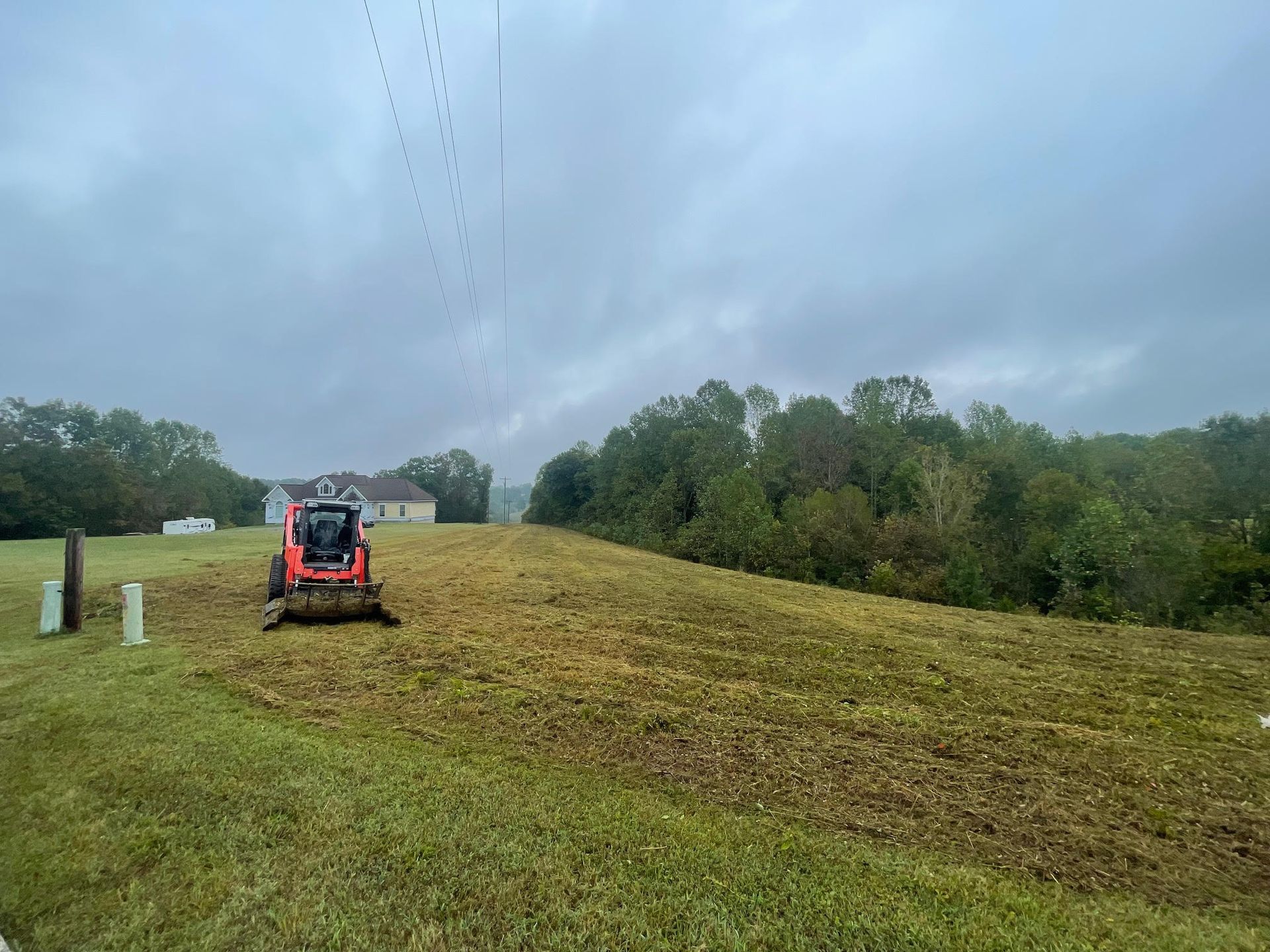 A tractor is cutting grass in a field on a cloudy day.