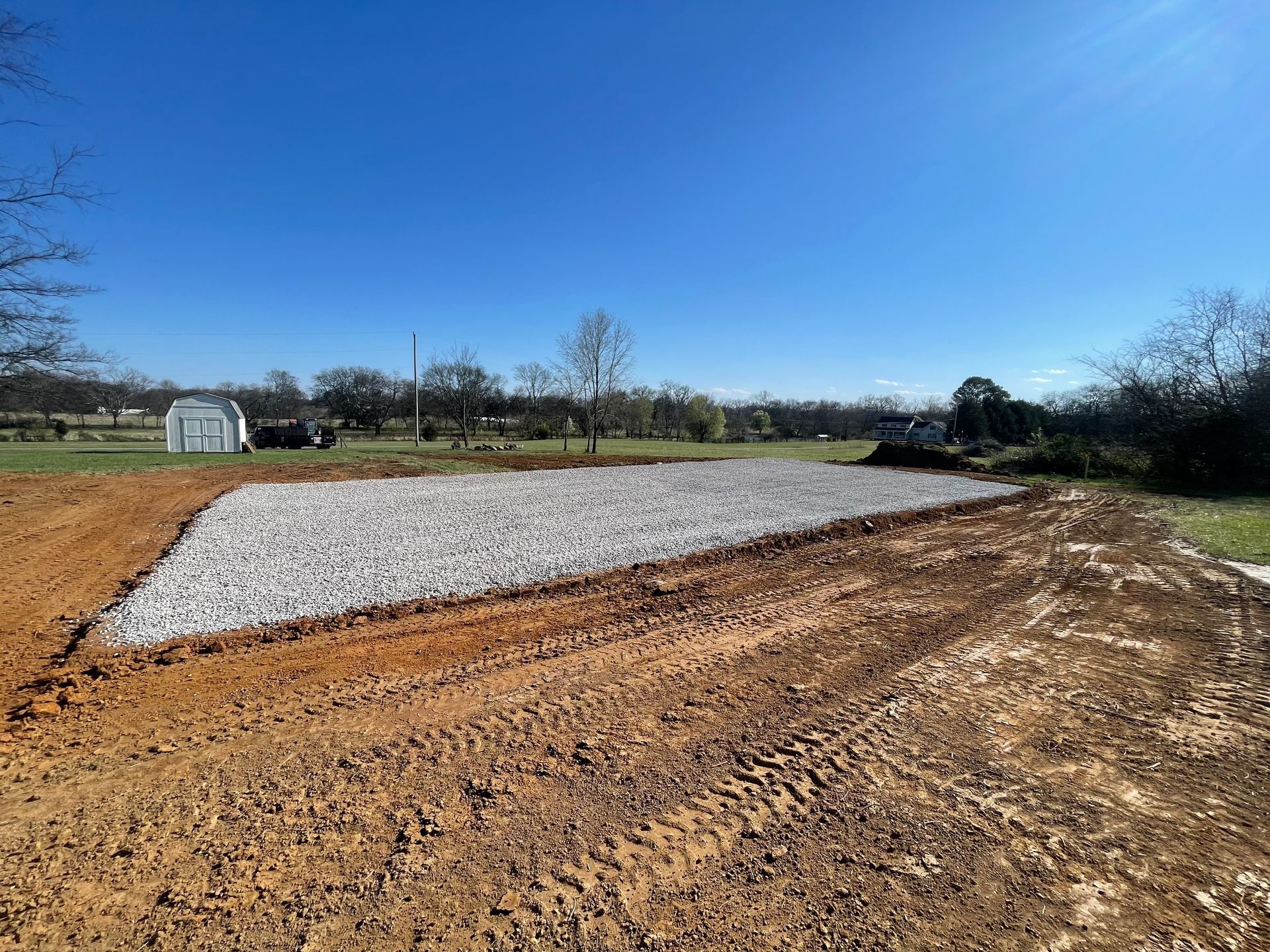 A dirt road leading to a house with trees in the background.