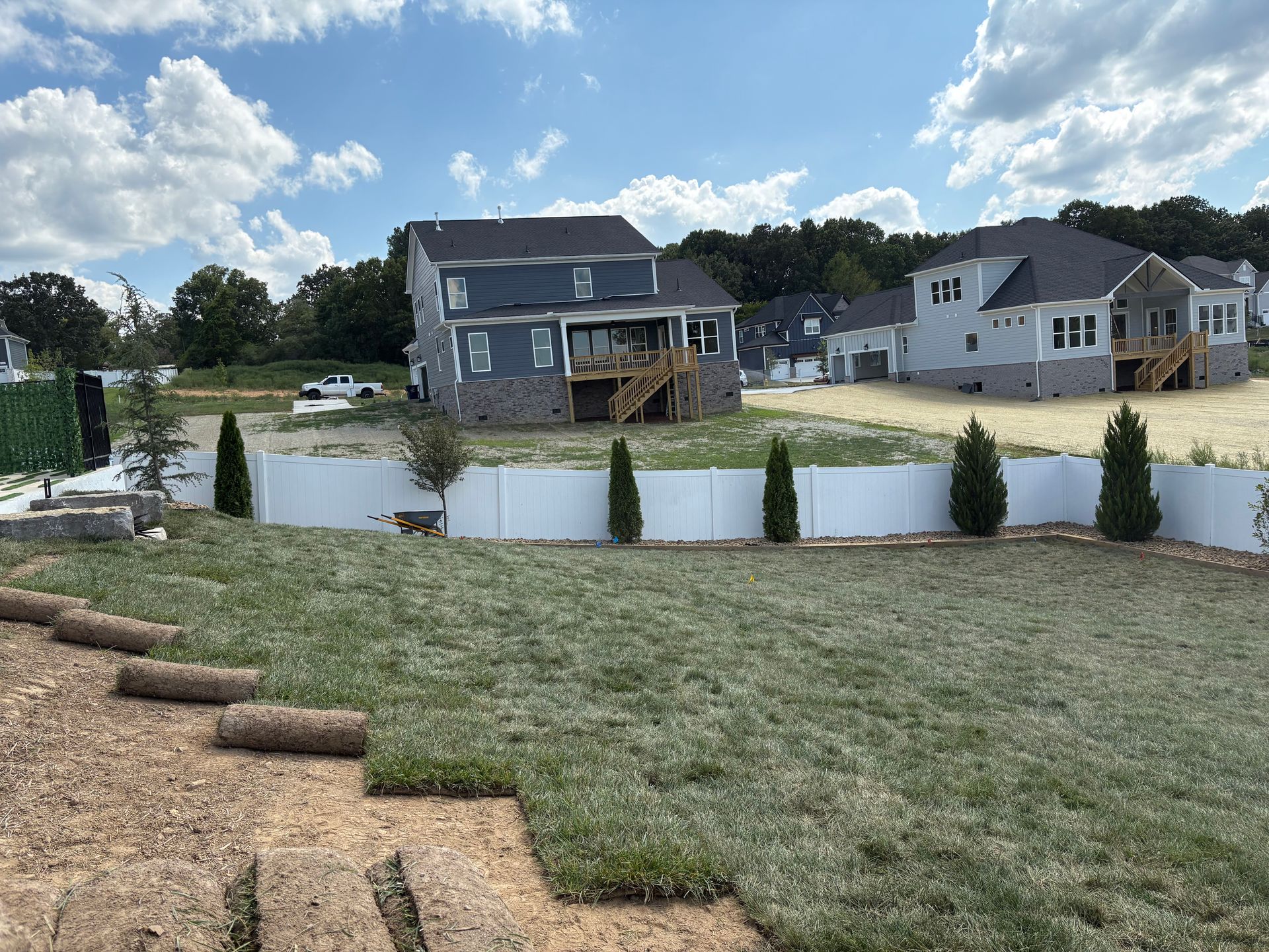 A lawn being sodded in front of new houses, white fence, cloudy sky.