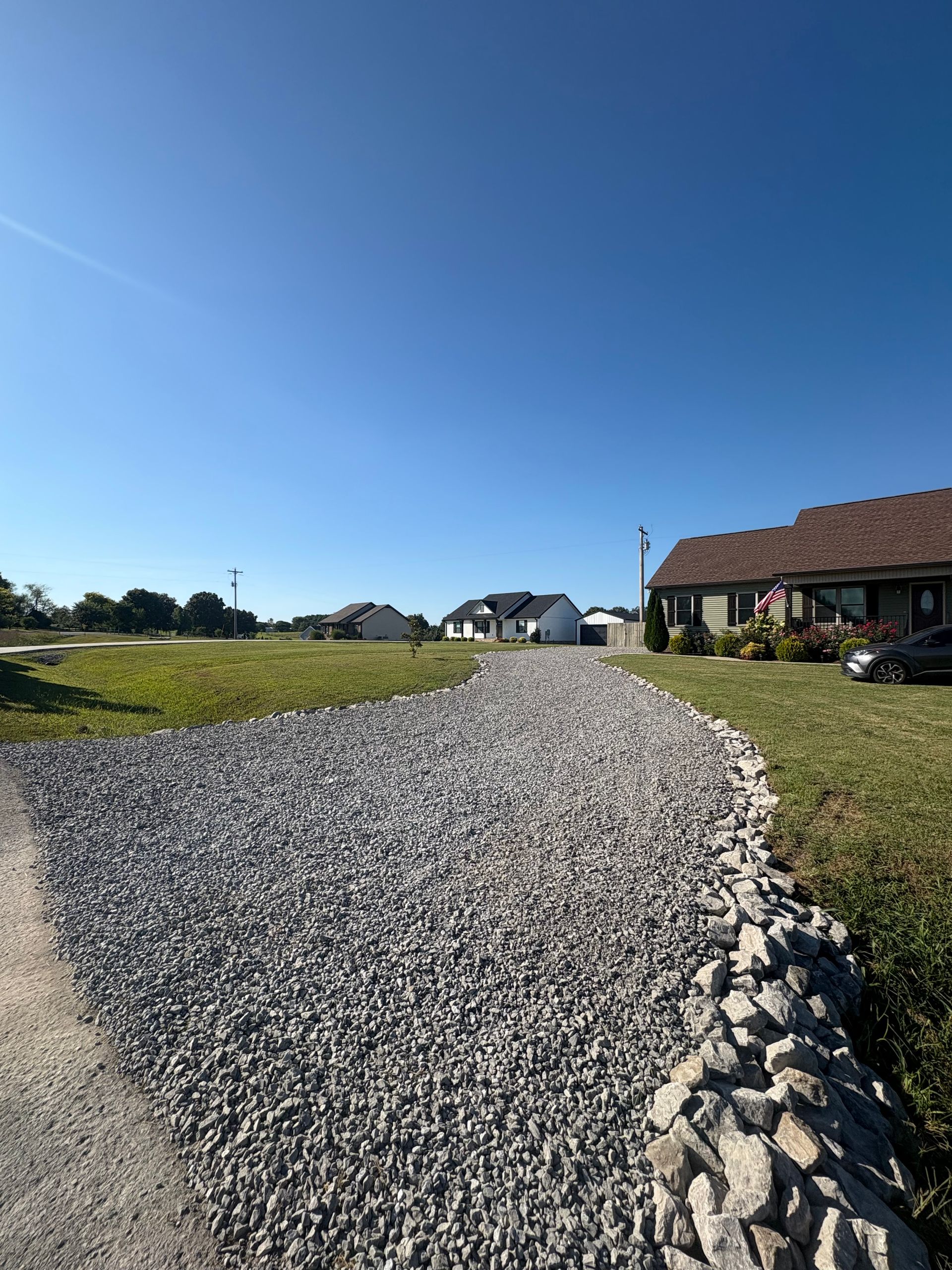 A red skid steer is parked on the side of a gravel driveway.