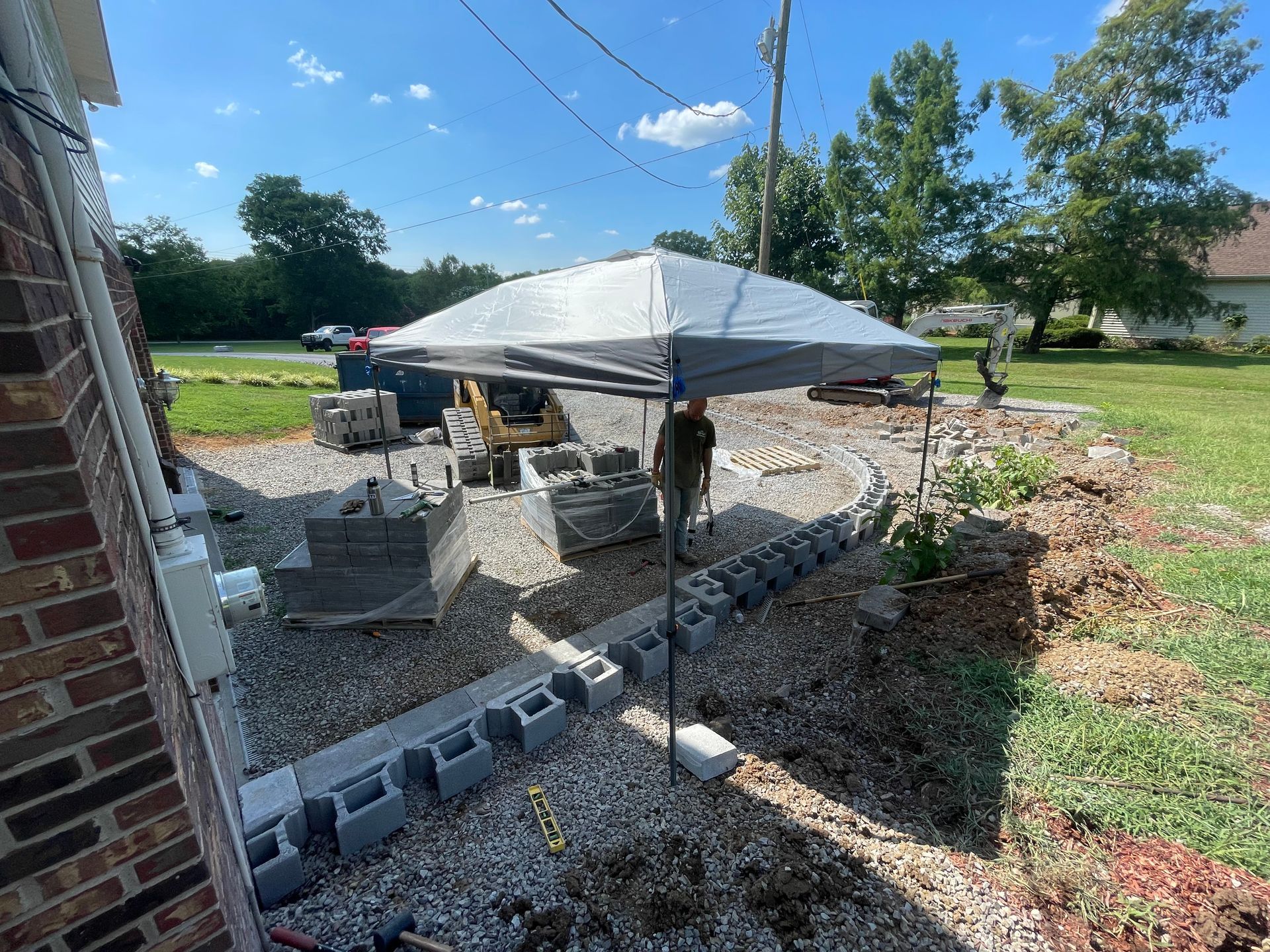 Construction of a brick patio: blocks, gravel, and a tent on a sunny day.