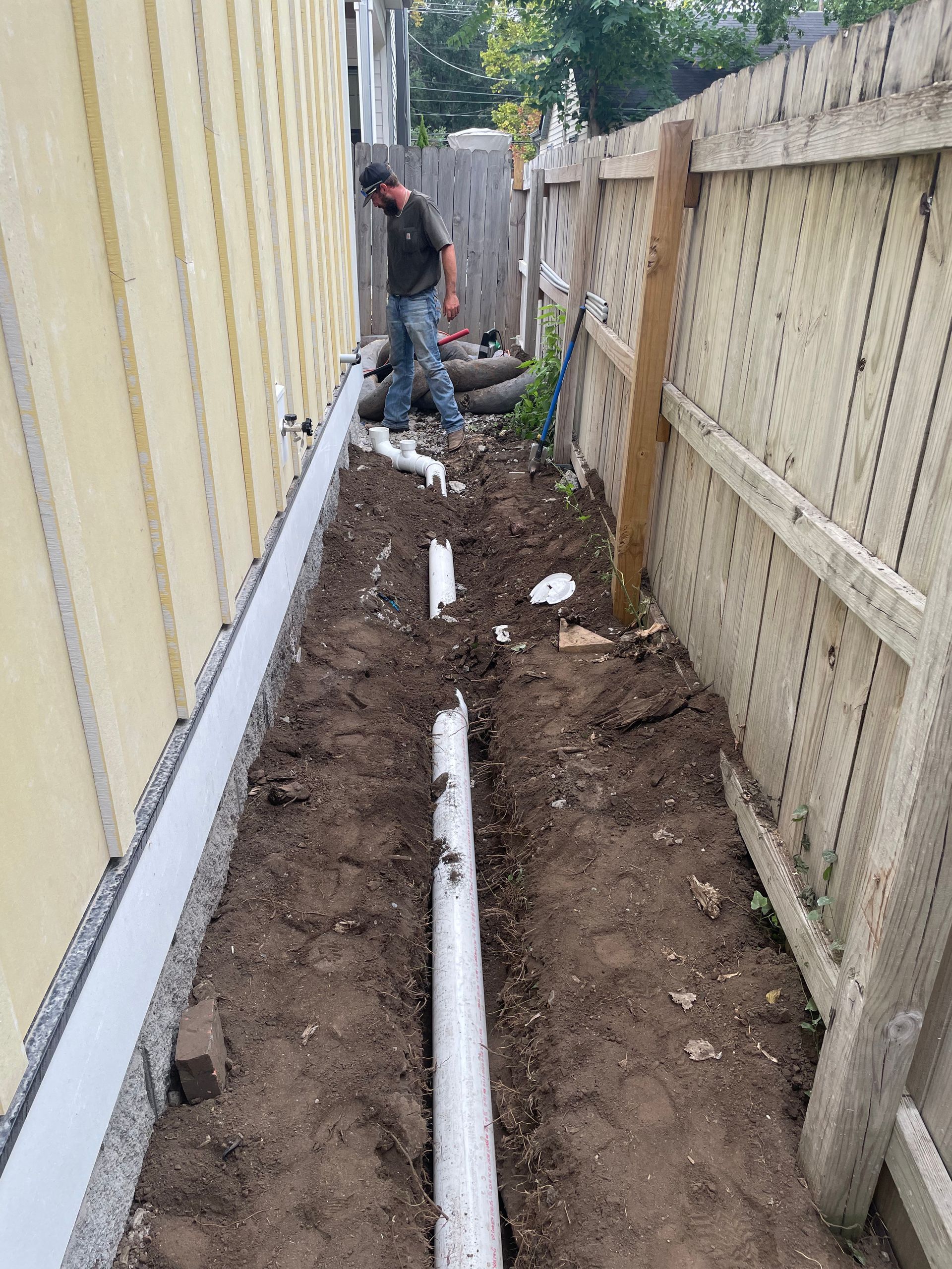 A man is digging a hole in the ground next to a fence.