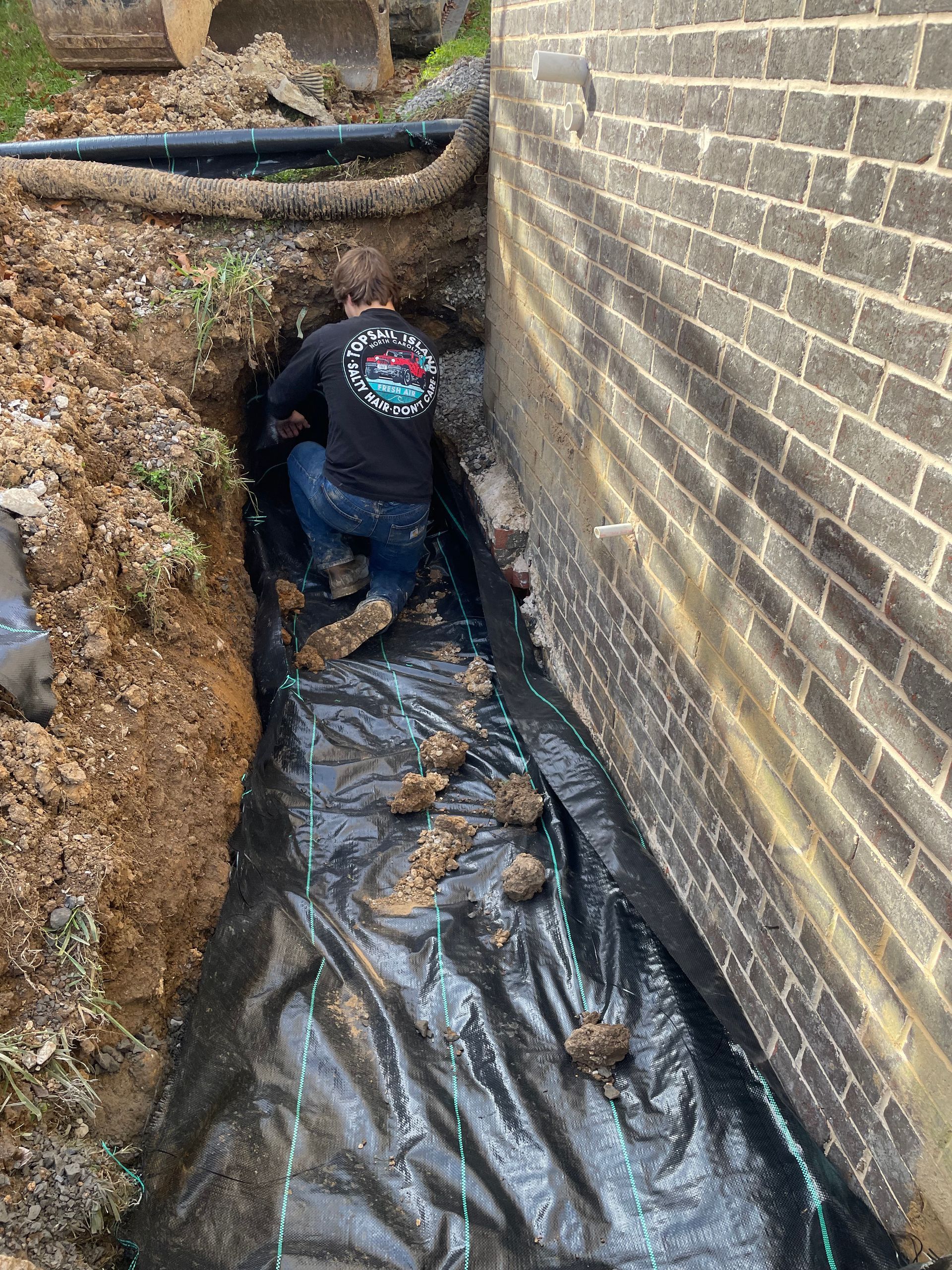 A man is kneeling in the dirt next to a brick wall.