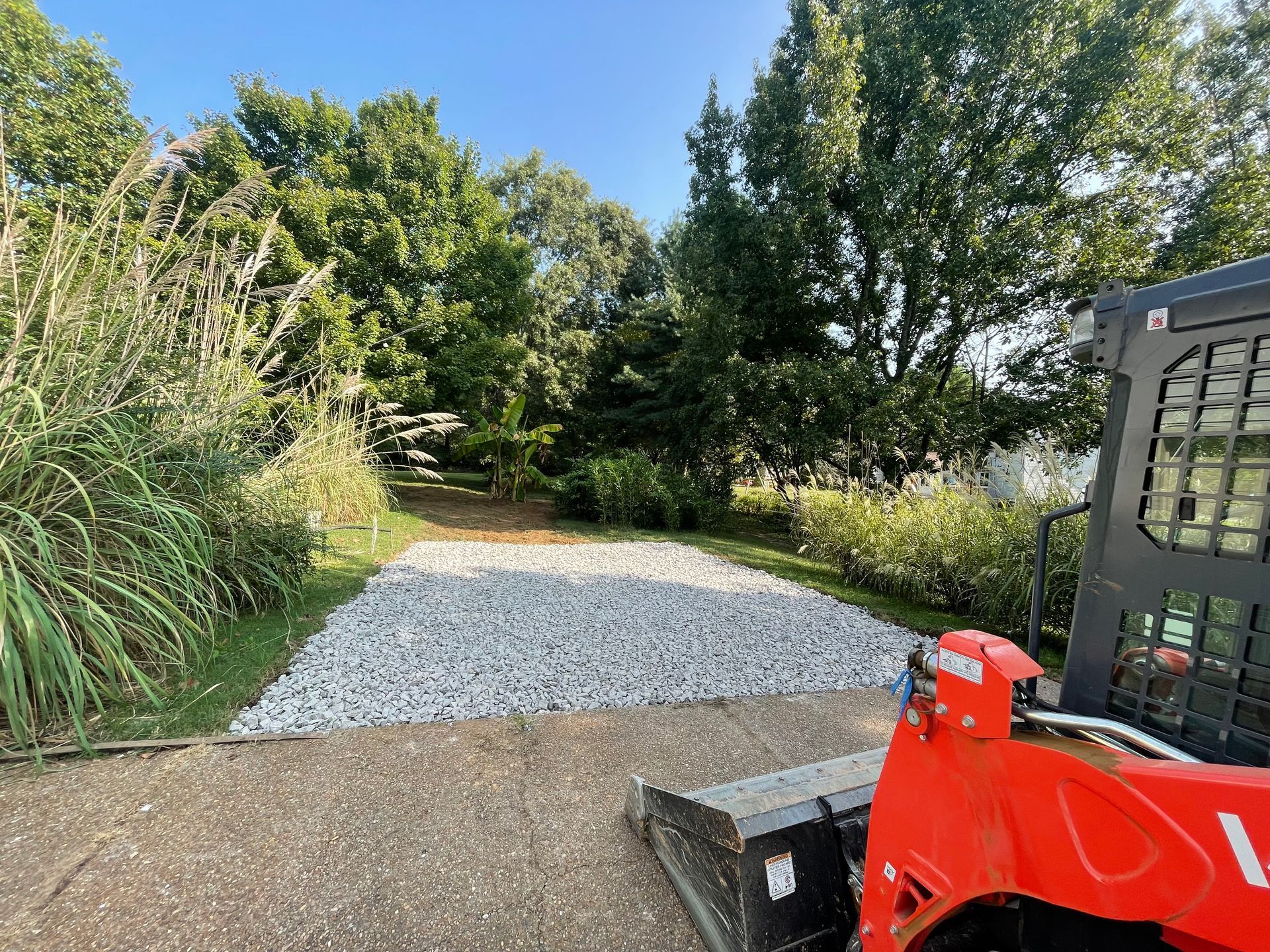 A red skid steer is parked on the side of a gravel driveway.