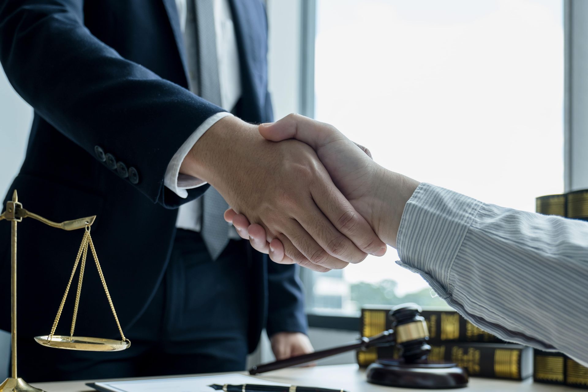 Two people in suits shake hands near scales of justice and a gavel.