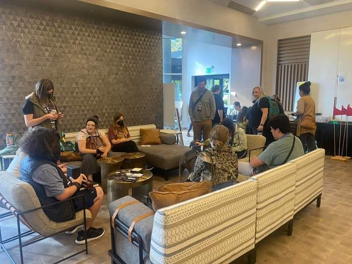 People seated and standing in a modern lounge area with couches, discussing.