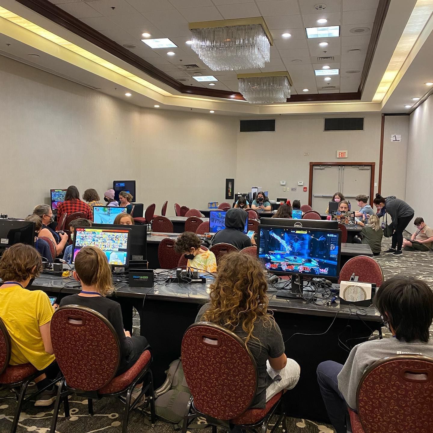 People playing video games at computers in a large convention room. Dark screens, many people in chairs.