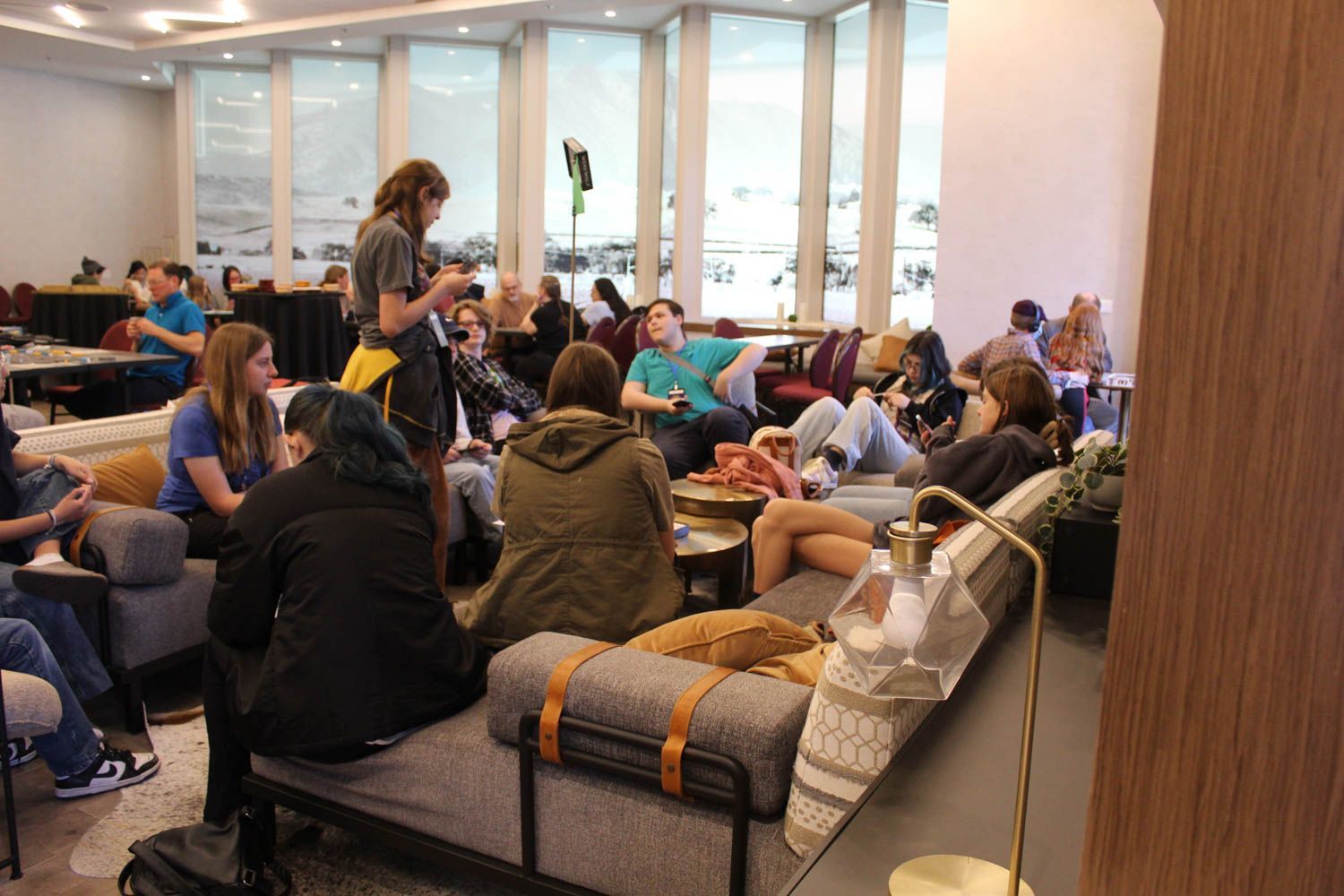 People lounging and chatting in a well-lit space with a large window overlooking a snowy landscape.