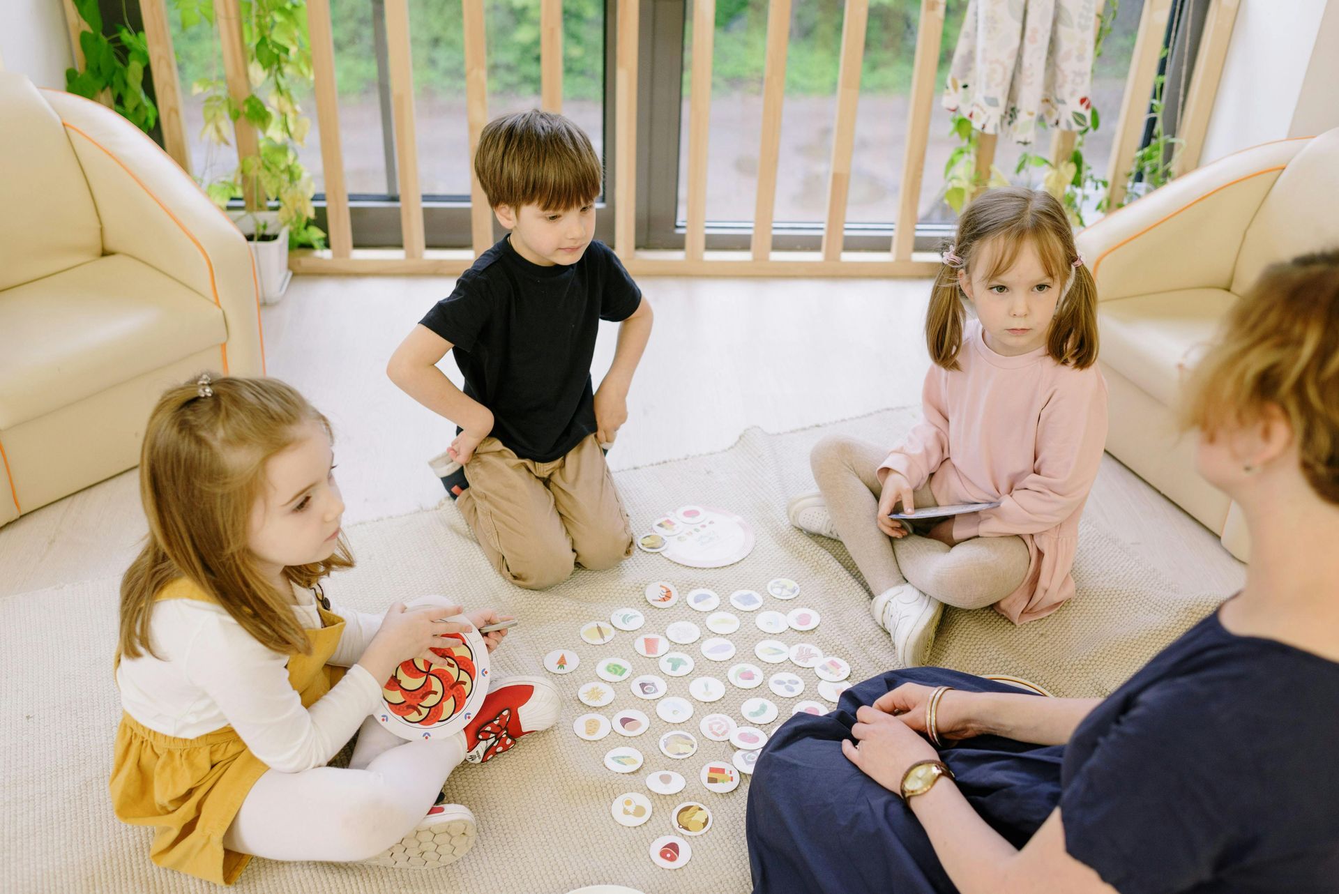 Four children and an adult playing a game on a rug indoors.