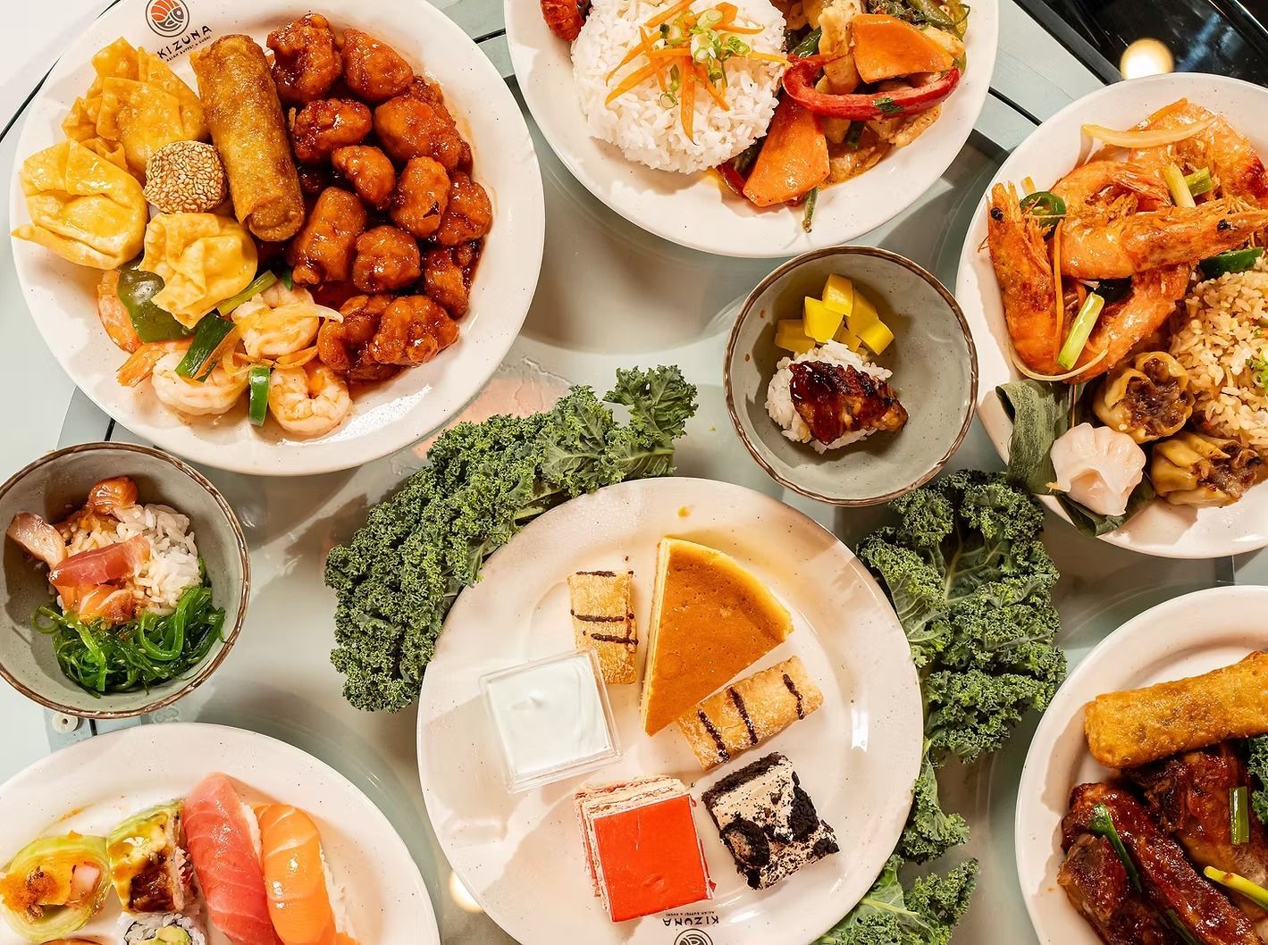 Overhead view of assorted plated appetizers and seafood dishes on a table with green garnish