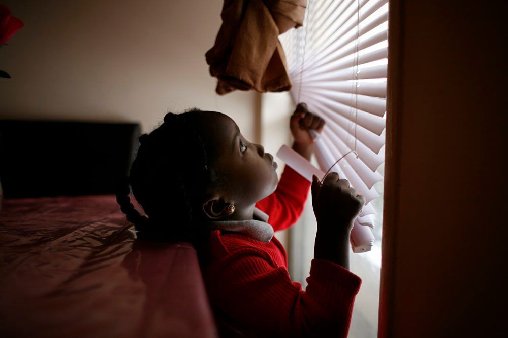 Omnia, Sawson's oldest daughter plays with the blinds in their new suburban home. Sawson and her family left the city because the rent was too high.