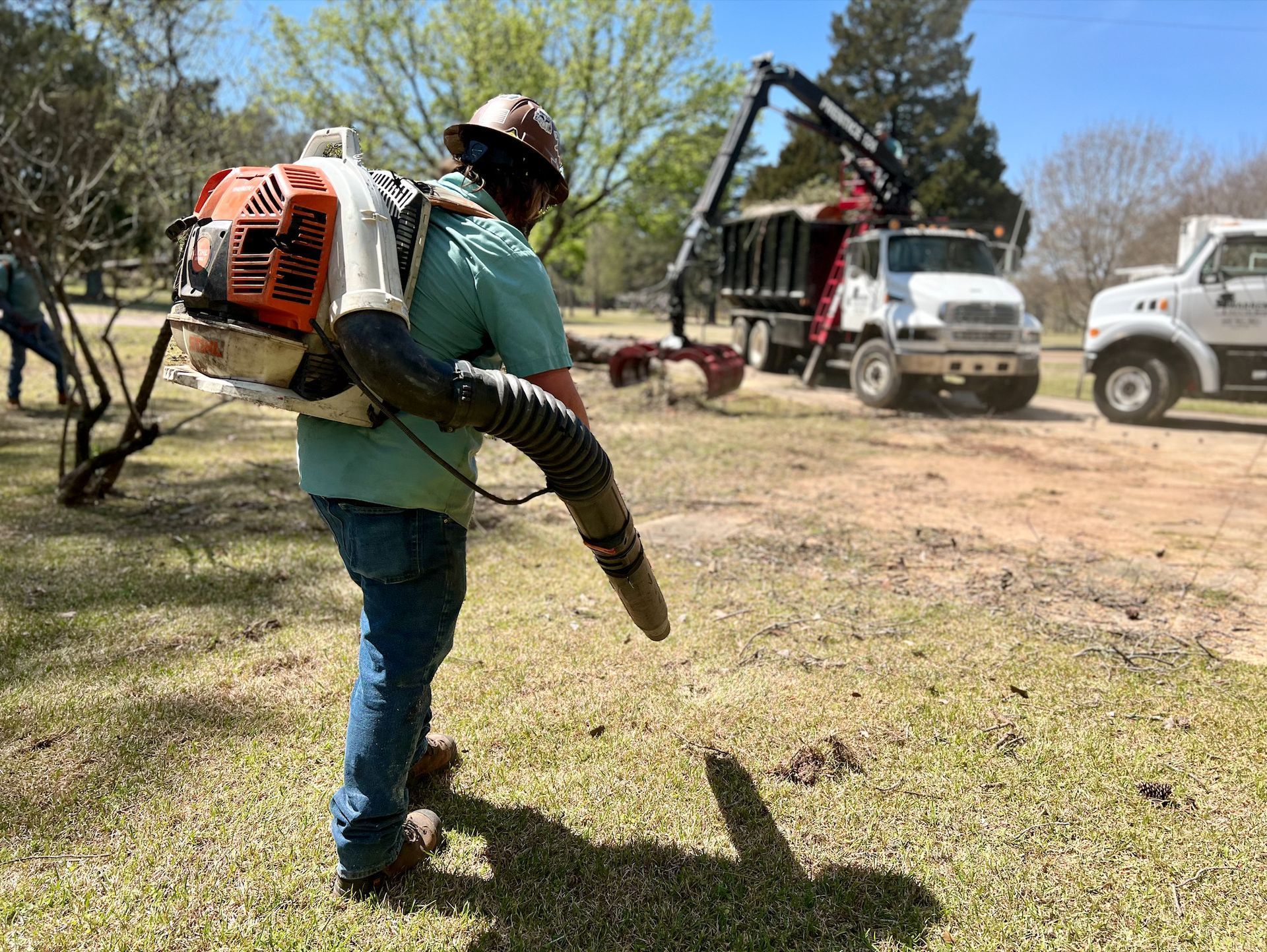 Person using a leaf blower on grass with work trucks in the background.